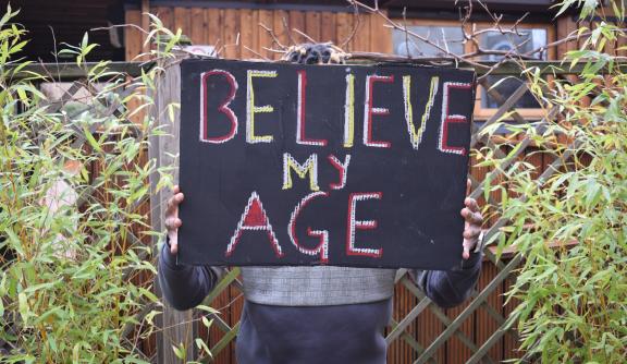 Person holding a placard that reads 'Believe my age'
